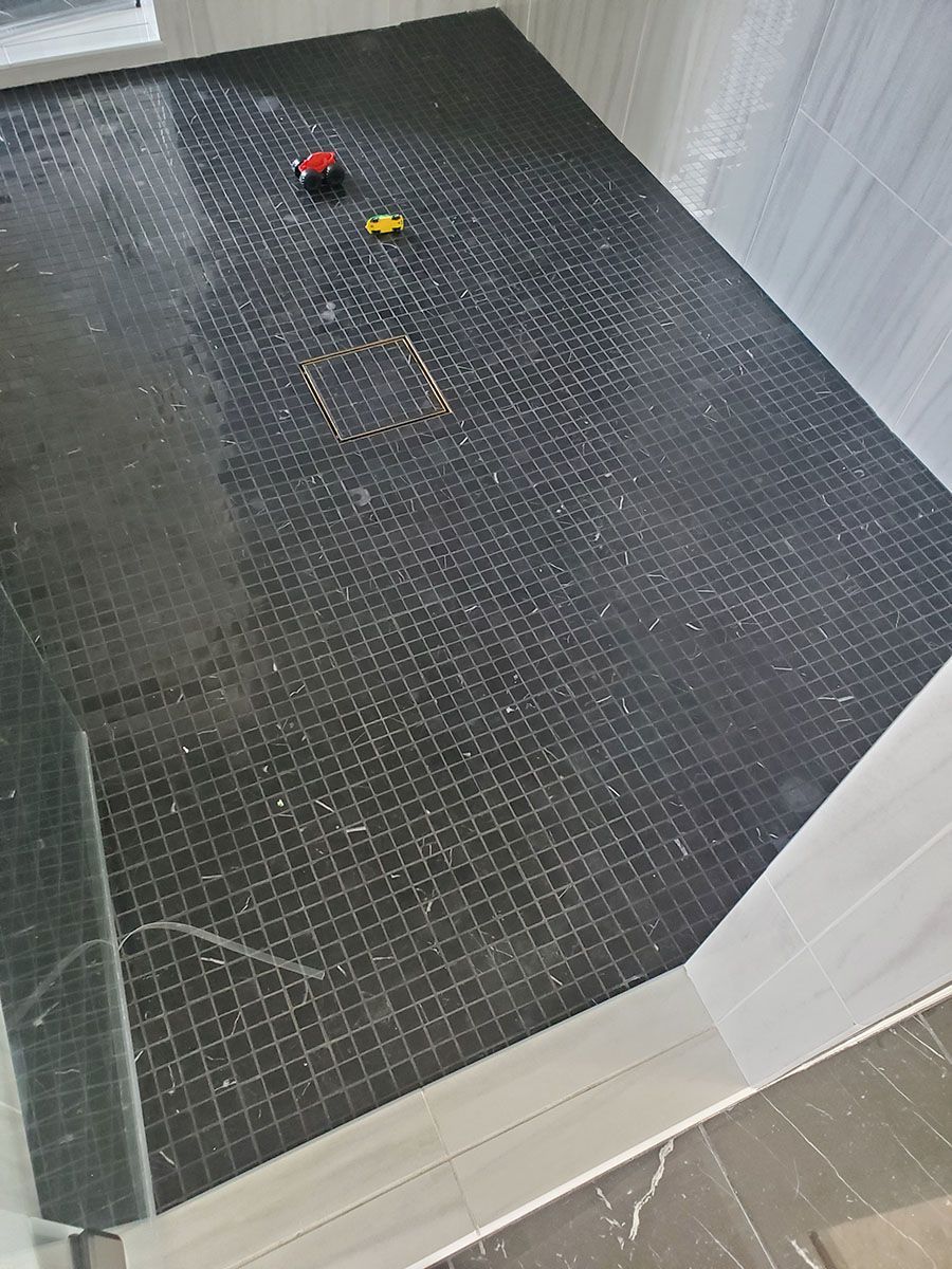 Black tiled shower floor with scattered debris and two small toy cars