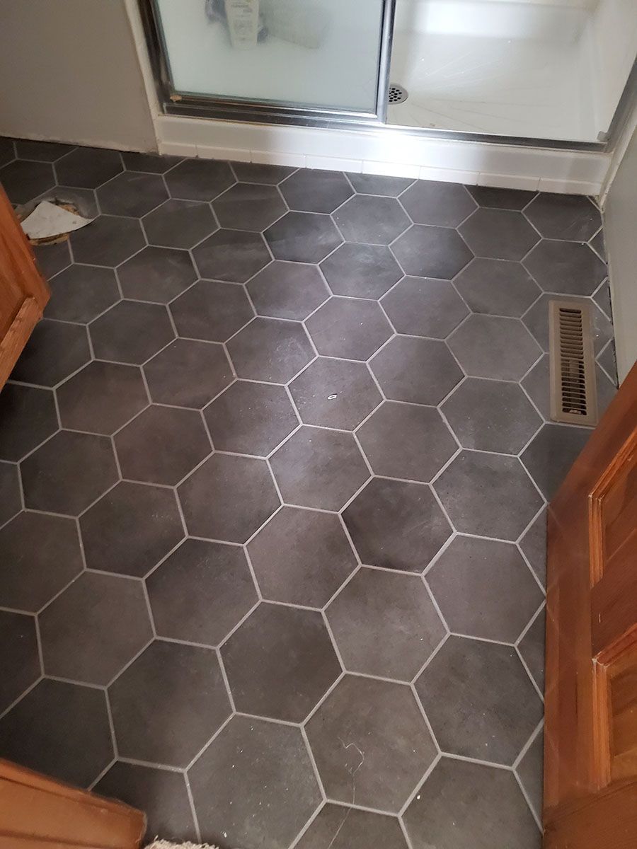 Dark gray hexagonal floor tiles in a bathroom, with a shower and wooden cabinet doors
