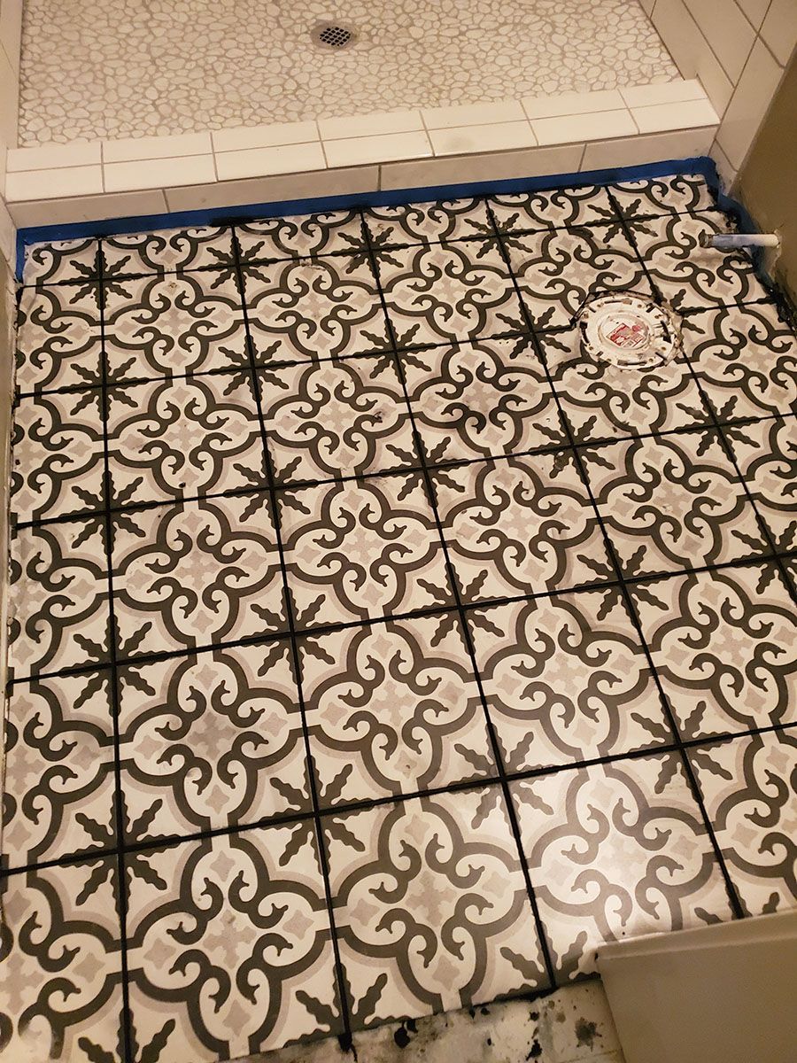 Shower floor with patterned tiles in gray and black, next to a white shower floor