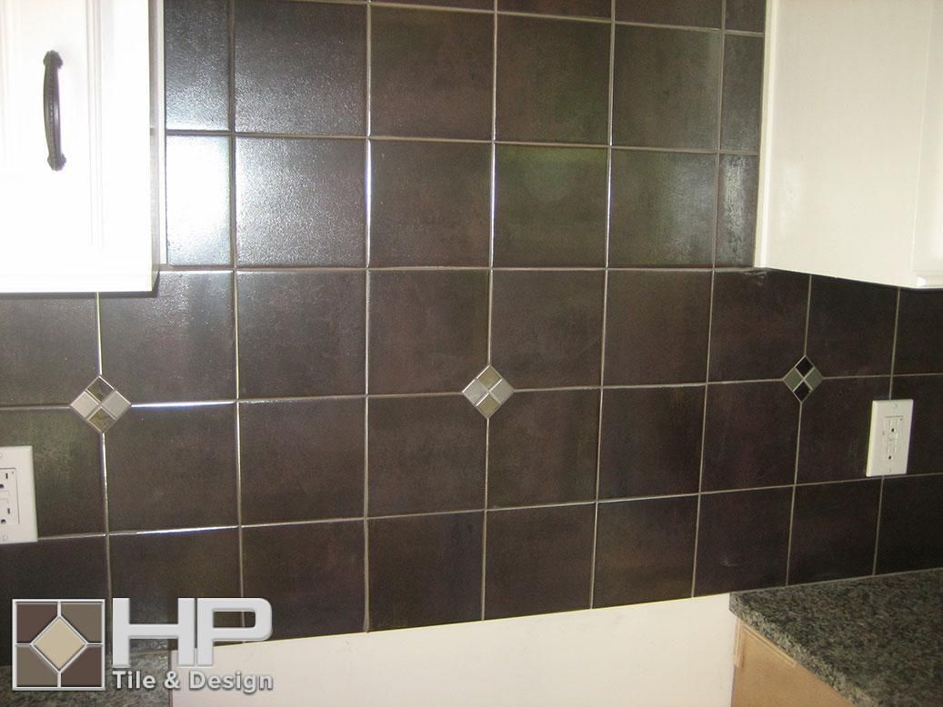Dark brown kitchen tile backsplash with diamond accents, white cabinets and outlets.
