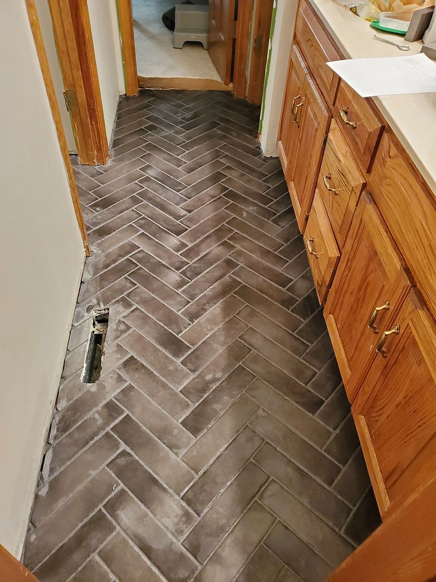 Herringbone patterned dark gray tile floor in a hallway with wooden cabinets and a doorway