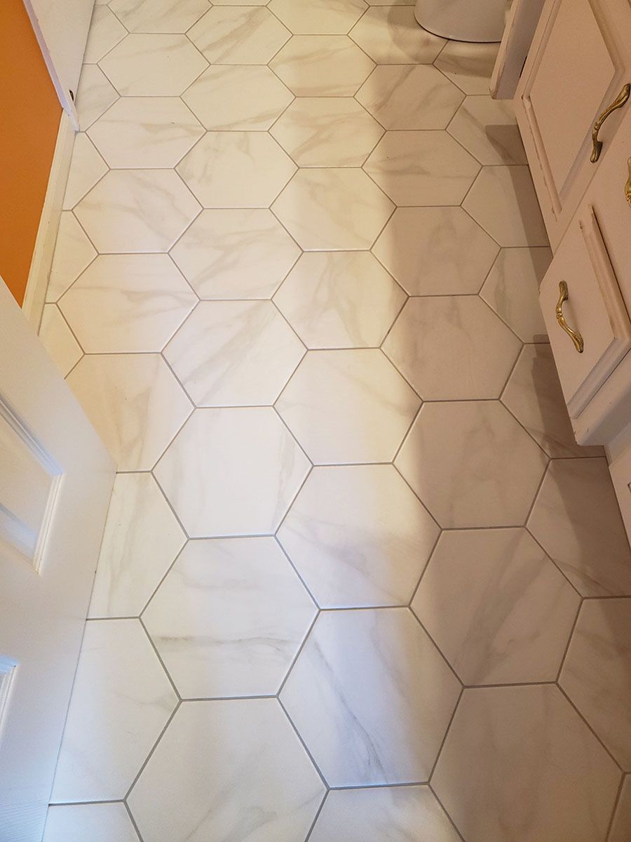 White hexagon tile floor in a bathroom, next to a white vanity with gold handles