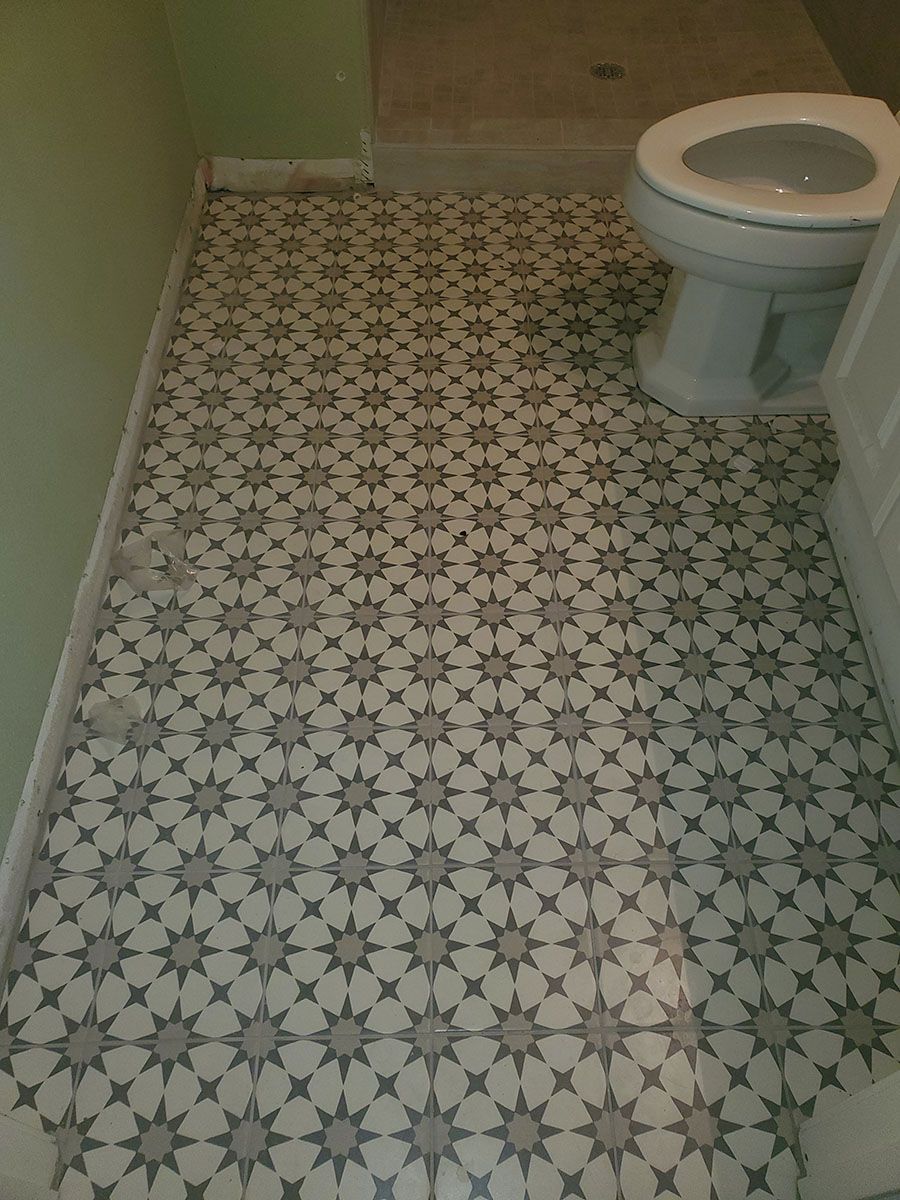 Bathroom floor with starburst patterned tiles, toilet, and light green wall