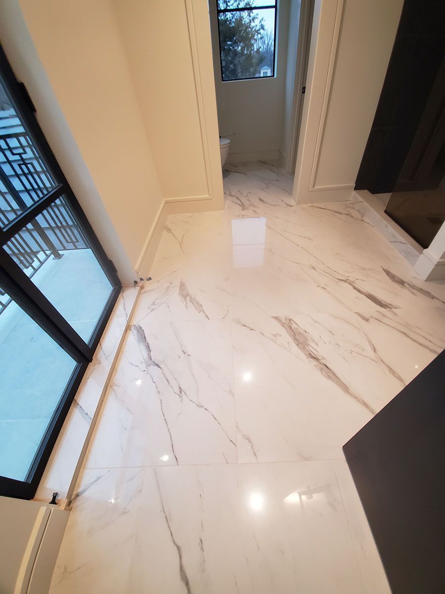 White marble floor with veining, leading towards a small room with a window and a toilet