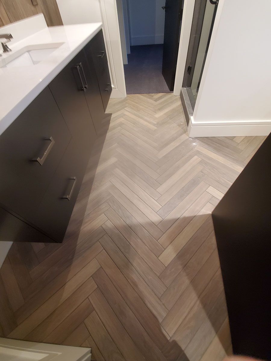 Herringbone wood floor in a bathroom, next to dark cabinets and a white countertop
