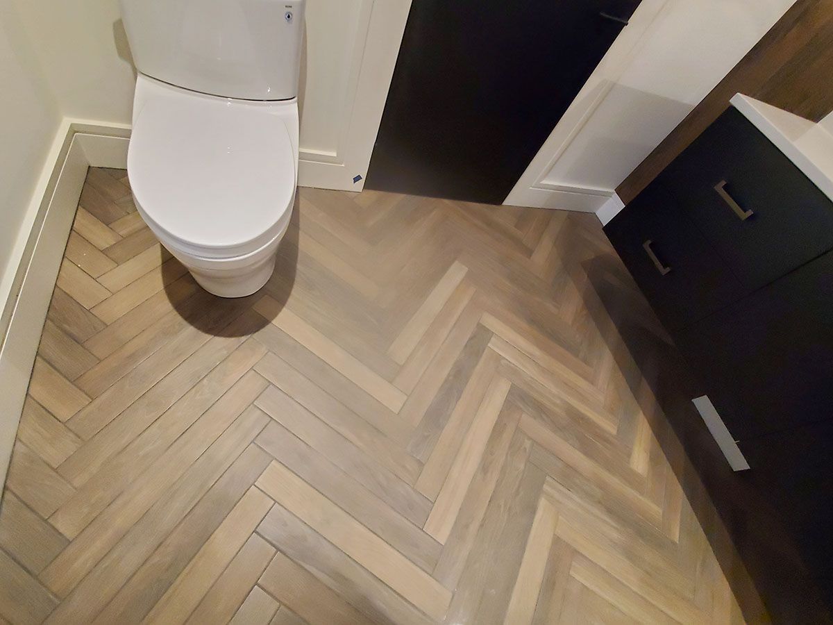 Toilet and dark cabinetry on a light brown herringbone patterned floor