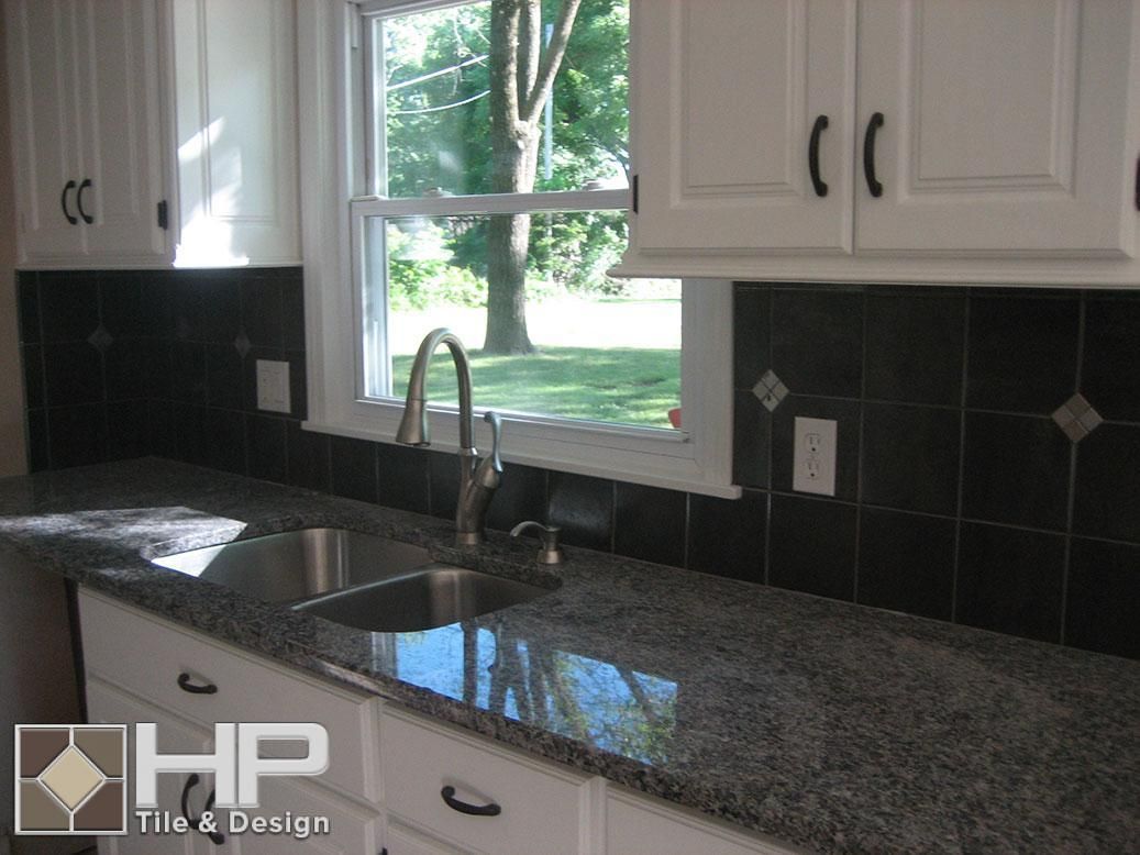Kitchen with white cabinets, black backsplash, granite countertop, and a window.