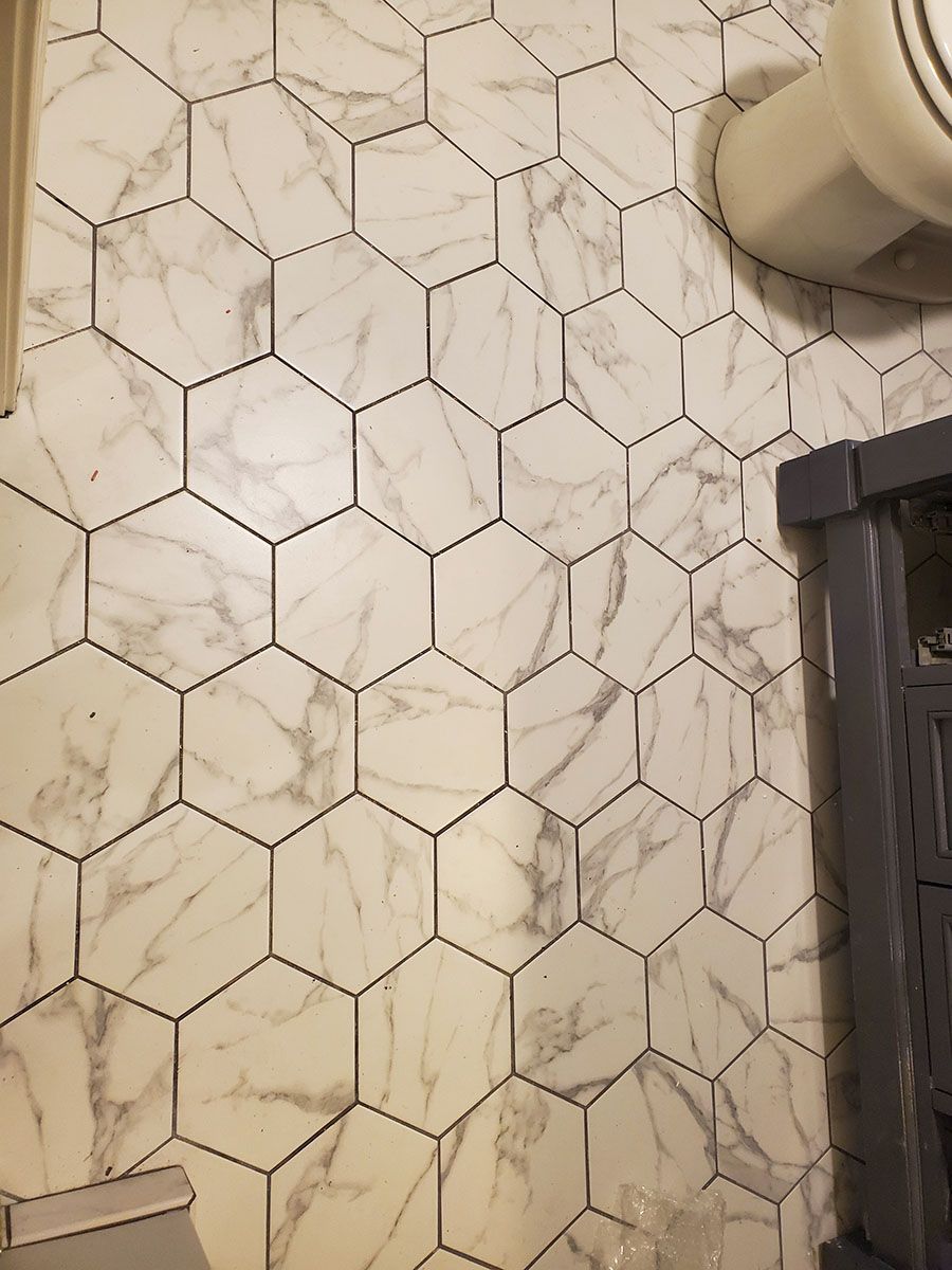 Hexagonal marble-patterned tiles on a wall, next to a toilet and a dark gray frame