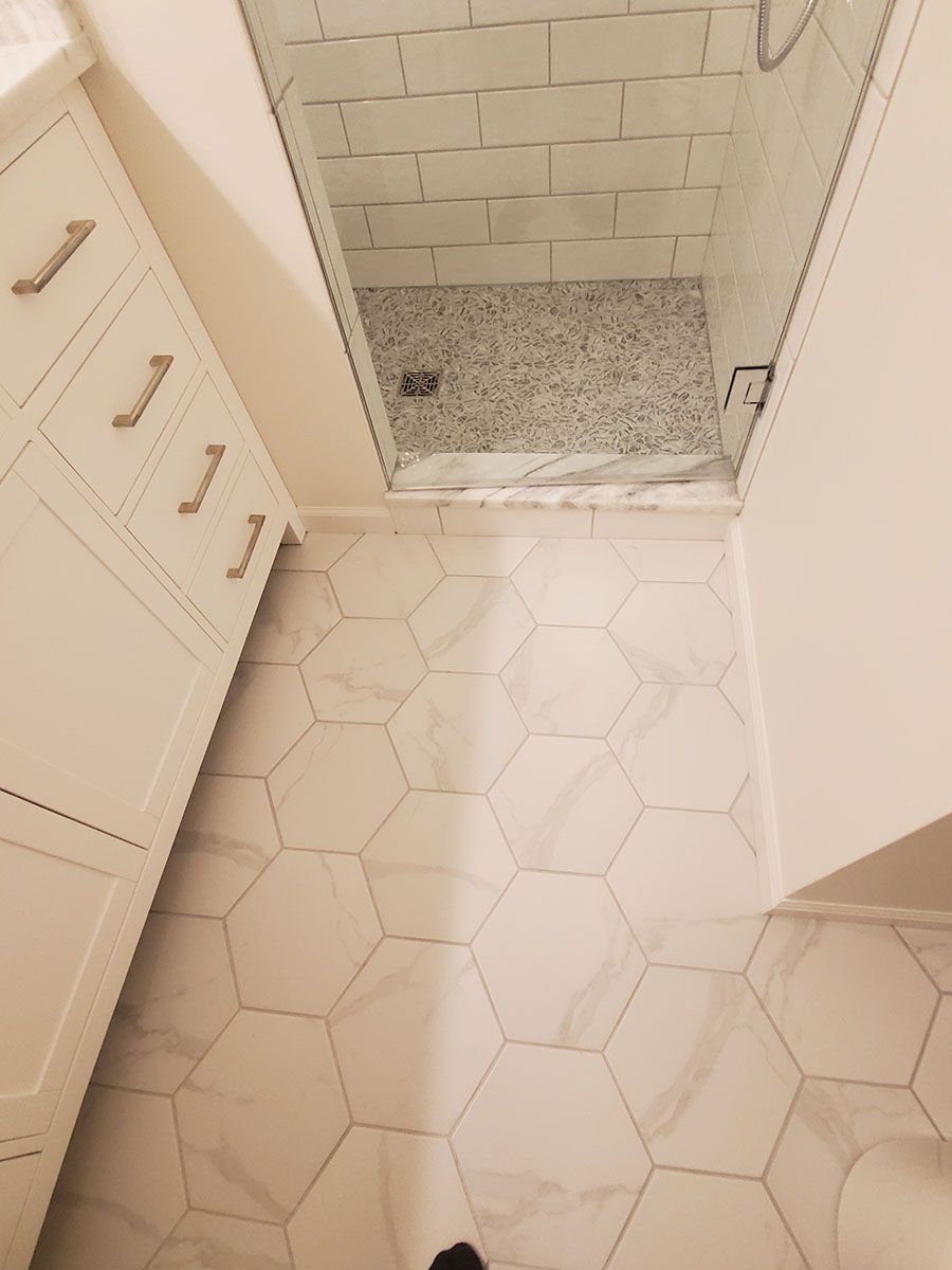 Bathroom with white hexagon floor tiles, walk-in shower, and white cabinets