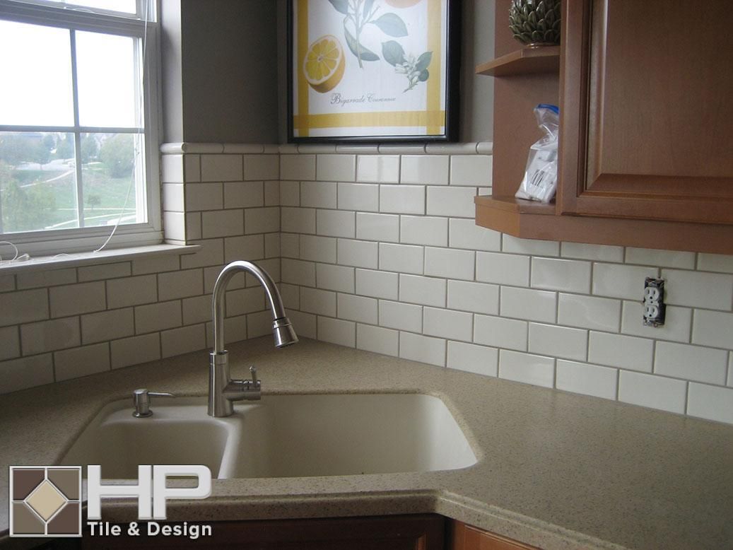 Kitchen corner with off-white subway tile backsplash, brown cabinets, and a sink. A framed lemon art piece hangs above.