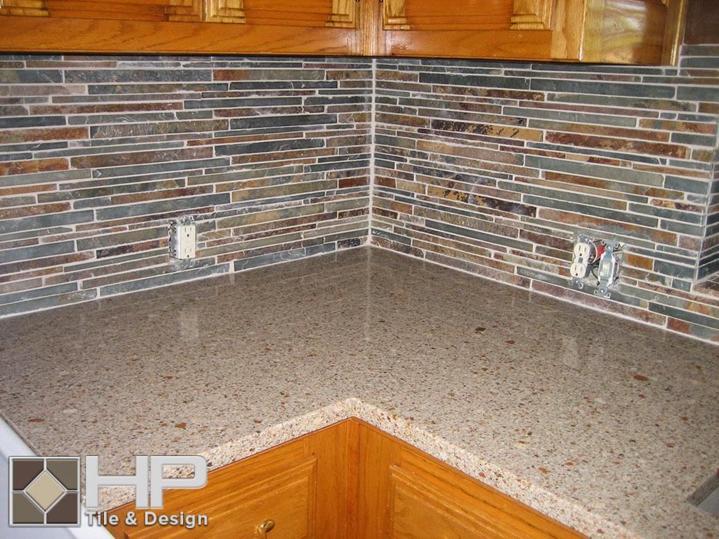 Kitchen corner with speckled countertop, tiled backsplash (brick pattern), and wooden cabinets.