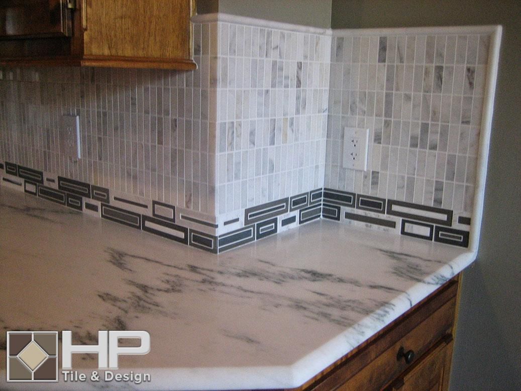 Kitchen with white marble countertop, gray and white tile backsplash, and wooden cabinets.