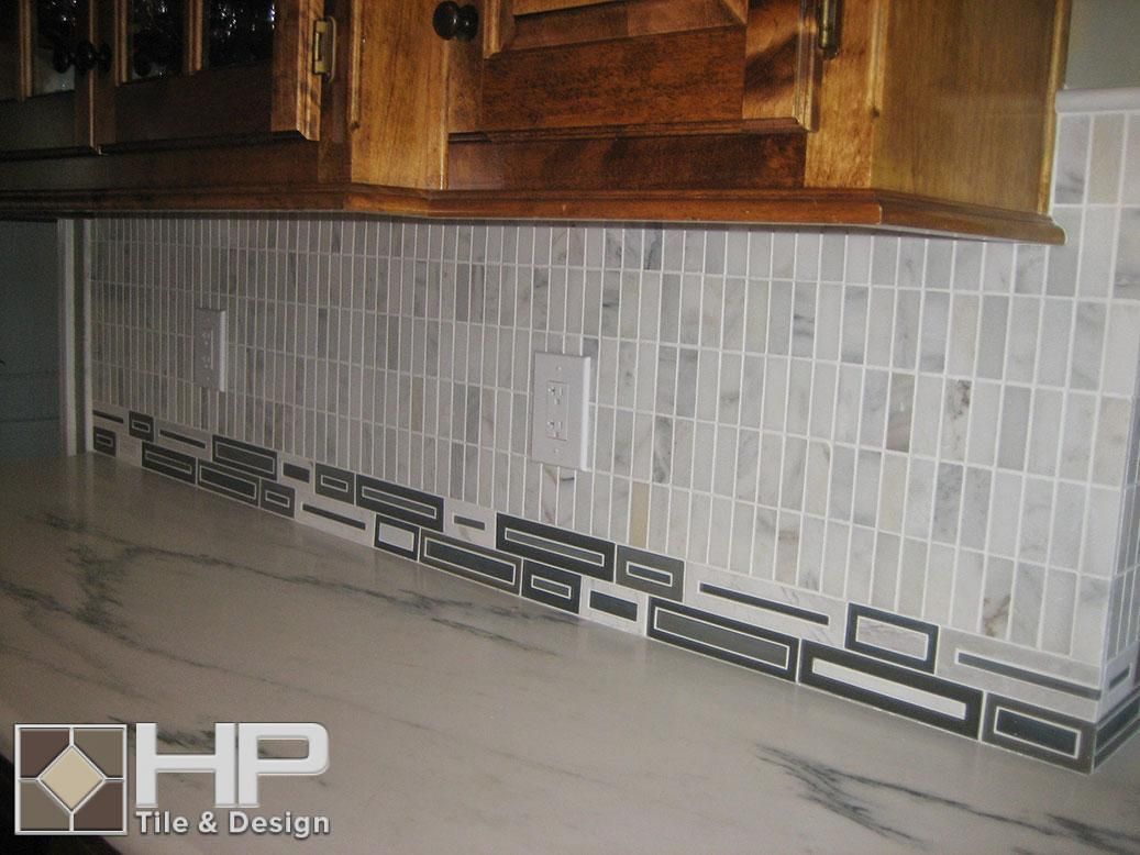 Kitchen backsplash with light-colored vertical tiles and decorative black and white trim along the countertop