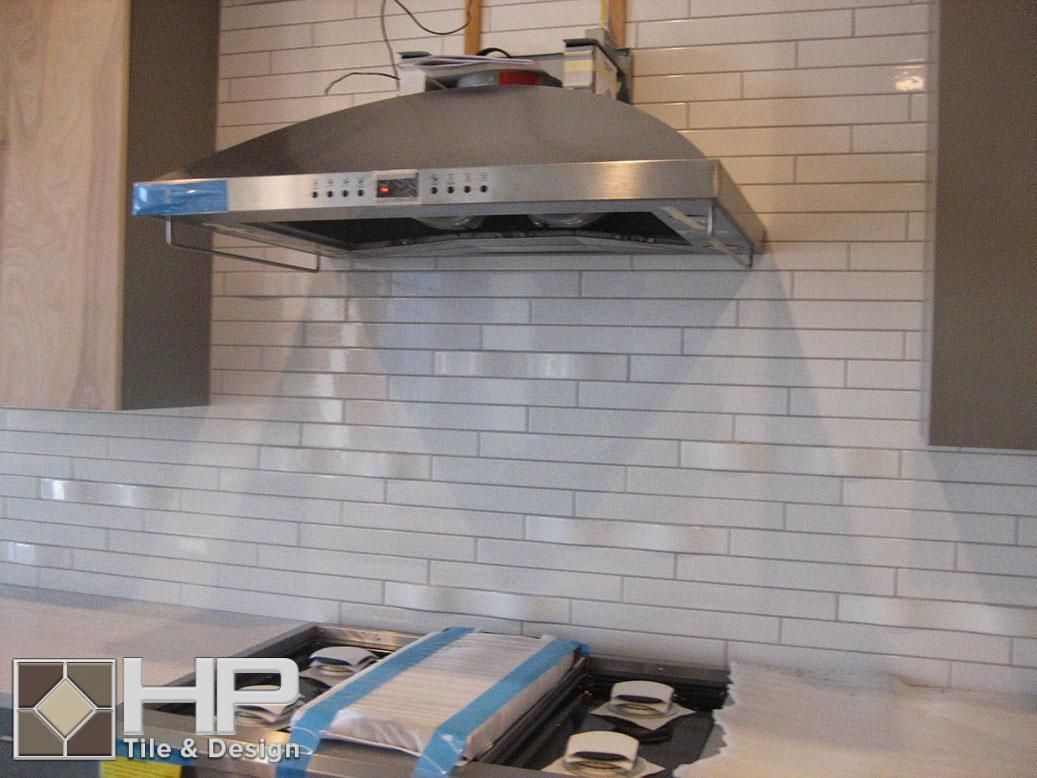 White subway tile backsplash with stainless steel range hood in a kitchen.