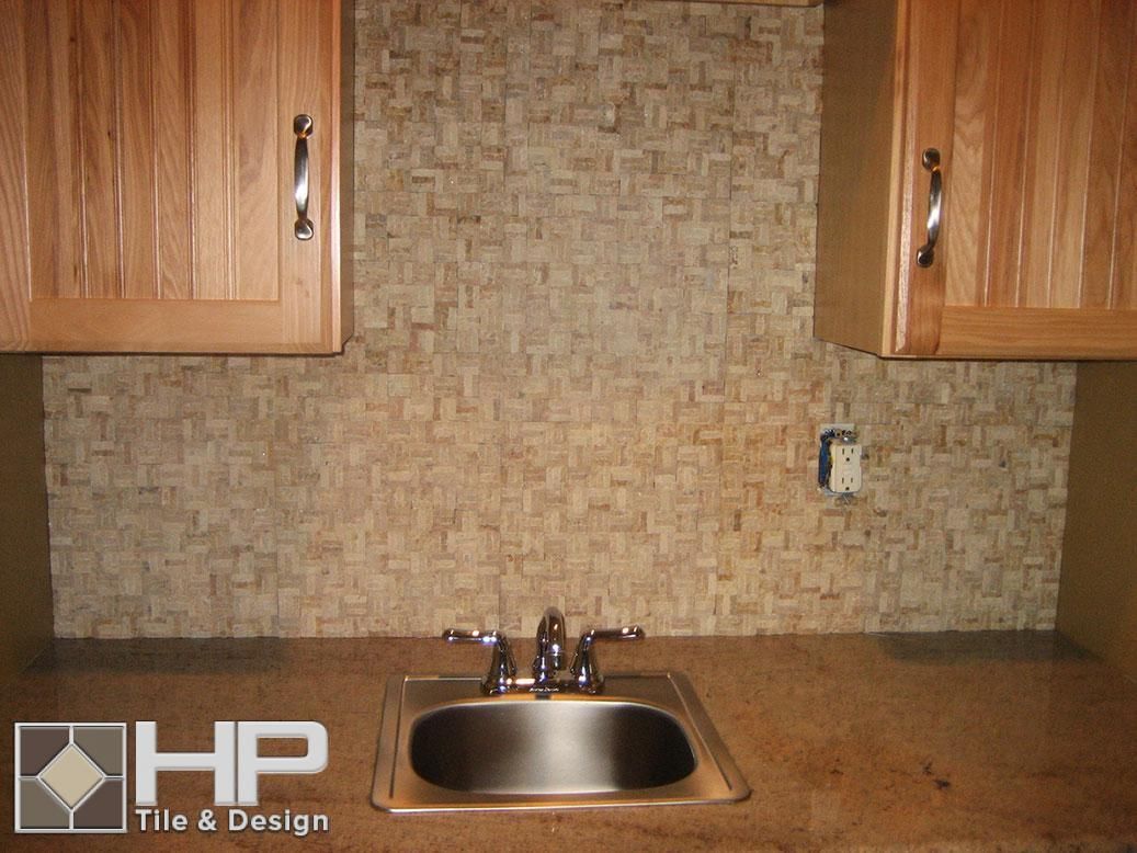 Small kitchen sink with stone tile backsplash, under wood cabinets.