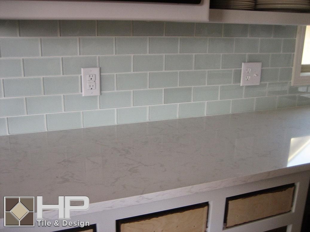 Light blue subway tile backsplash with light gray countertop and white outlets.