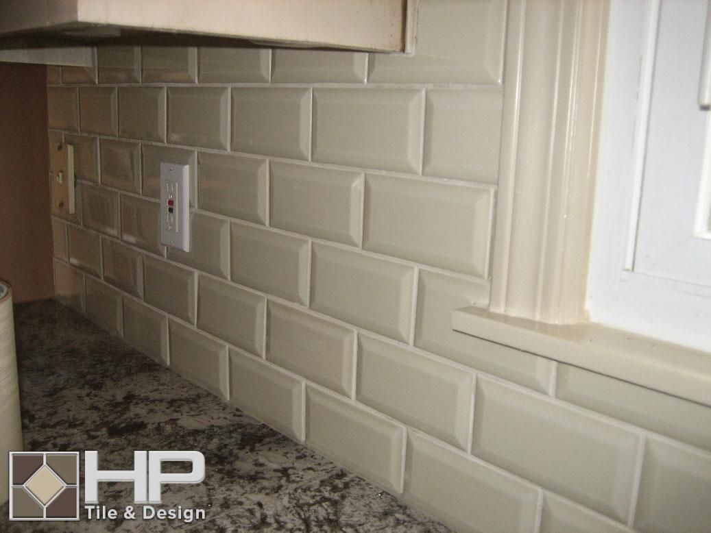 Off-white subway tile backsplash in kitchen with granite countertop and window trim.