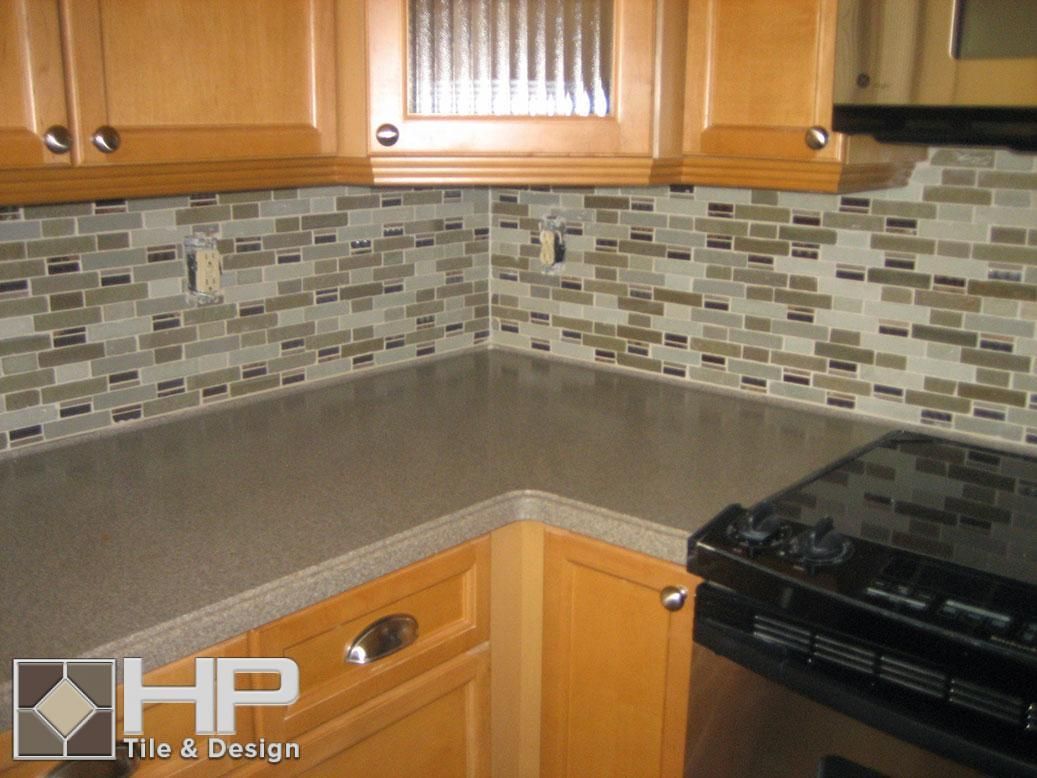 Kitchen corner with light wood cabinets, gray countertop, and mosaic backsplash, near a stove.