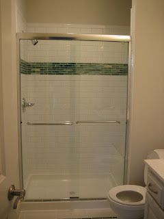 Bathroom shower with sliding glass doors, white shower base, and green mosaic tile accent
