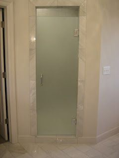 Frosted glass shower door set in a marble-tiled alcove, with a handle, and a hinge