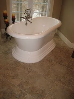 Freestanding white bathtub on a tiled floor, near a window