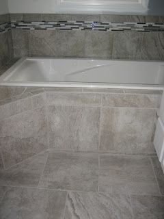 Bathroom with a gray tile floor, tub, and mosaic tile accent