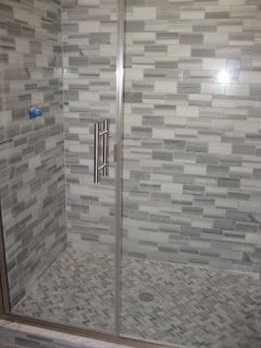 Shower with gray and white mosaic tile walls and floor, glass door, and silver handle
