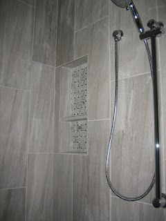 Grey tiled shower with built-in shelf. Silver showerhead and handheld shower.