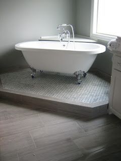 Clawfoot bathtub on a tiled platform in a bathroom next to a window and cabinet.
