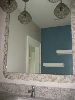 Mirror with a decorative stone border above a bathroom sink. Gray and blue walls with pendant lights.