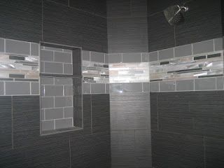 Dark gray tiled shower with a decorative horizontal band of lighter tiles and a built-in shelf.