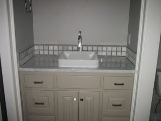 Bathroom vanity with a white sink, grey cabinets, and square tile backsplash