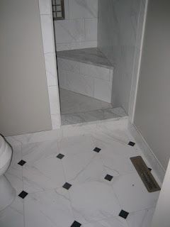 Bathroom with white marble floor, black accent tiles, and a walk-in shower with a bench