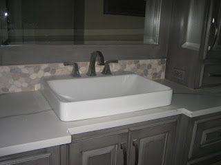 White rectangular sink on gray cabinet, with a gray faucet and speckled backsplash