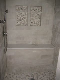 Shower with gray tile walls, pebble floor, built-in bench, and two decorative stone tile inserts