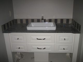 White vanity with gray countertop and vessel sink. Vertical tile backsplash
