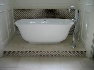 Freestanding white bathtub in a tiled alcove, with chrome faucet
