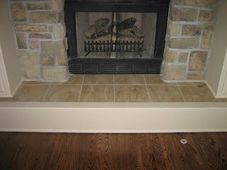 Fireplace with stone surround and tiled hearth, set against hardwood flooring.