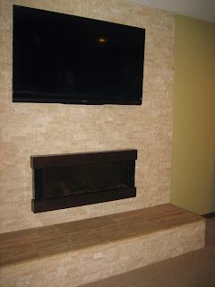 TV and fireplace mounted on a beige stone wall with a matching bench; a corner is green.