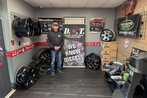 Person standing in a small tire shop showroom with custom wheels, boxes, and signage displayed around them