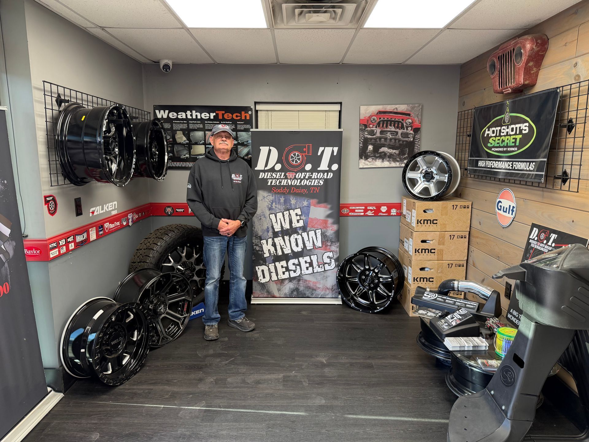 Person standing in a tire shop display area with rims, posters, and stacked boxes