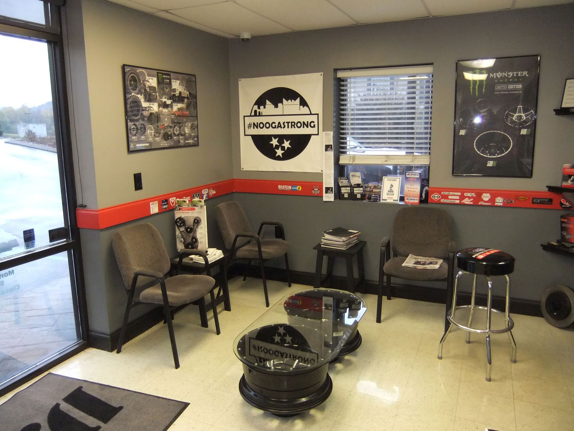 Small waiting area with black chairs, stools, wall art, and a red stripe along beige walls.