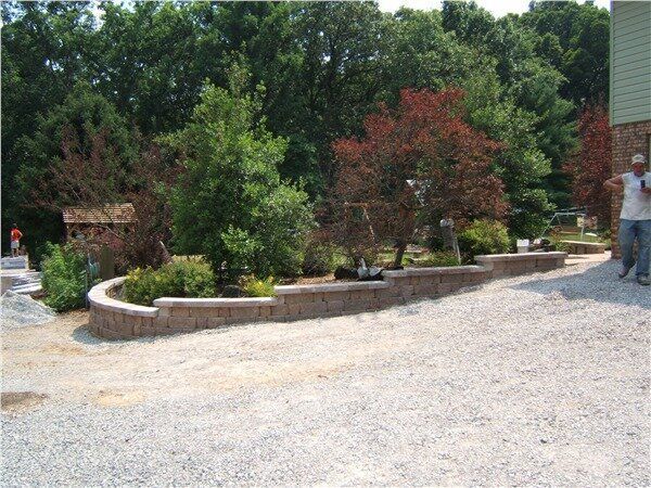 A man standing in a gravel driveway next to a brick wall