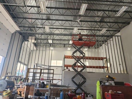 Warehouse interior with scissor lift, metal framing, and construction equipment under a high ceiling
