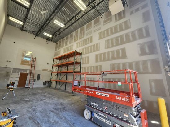 Industrial interior with drywall, scaffolding, and a red scissor lift in a large warehouse space