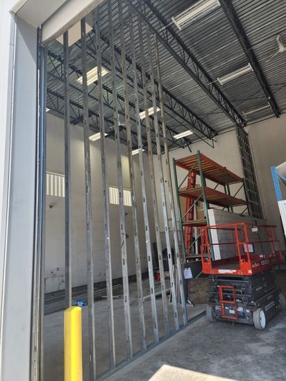 Warehouse interior with steel framing, a yellow bollard, and a red scissor lift under construction.