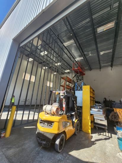 Yellow forklift lifting goods in a warehouse loading bay with a partially open roll-up door