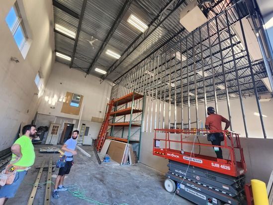 People working inside a warehouse with metal shelving, a red lift platform, and exposed ceiling framing