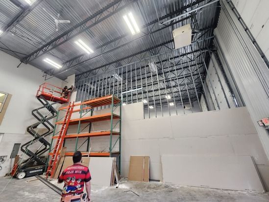 Warehouse interior with tall orange shelving, scissor lift, and a person in a red shirt near a partially built wall