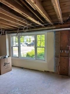 Unfinished room with exposed ceiling beams, large window, and bare drywall during renovation